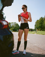 Woman standing next to car holding water bottle. 