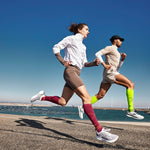 Two people running next to each other with blue skies behind him. 